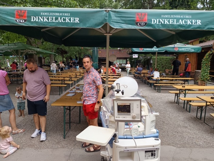 Ein grüner Sonnenschirm mit der Aufschrift Dinkelacker vor Bäumen.