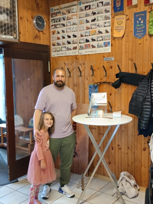 Ein Mann und ein Mädchen stehen lächelnd in einem Raum mit Holzwänden und Kaninchenpostern.