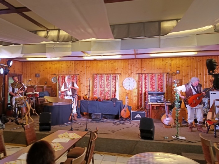 Eine Band spielt auf einer Holz-Bühne mit Instrumenten, umgeben von roten Vorhängen und einer Uhr.