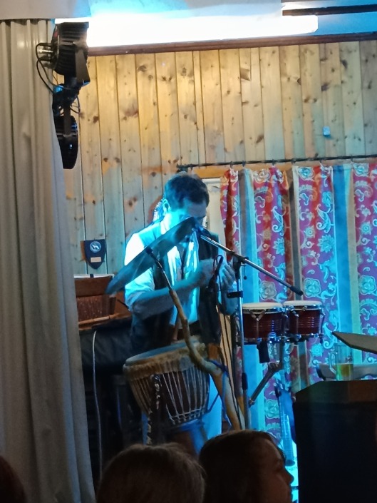 Musiker spielt Percussion vor Holzwand mit blauen Lichtstrahlen.